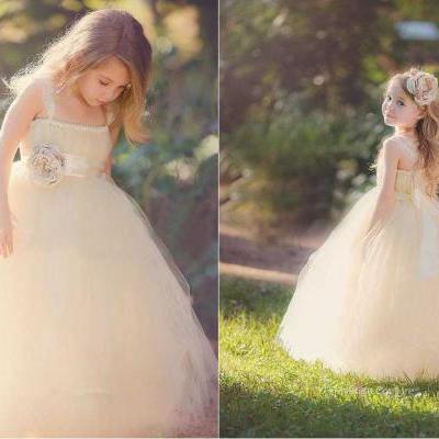 Floor length custom flower girl dress. Blush tulle puffy ball gown skirt adds dimension for a stunning look. Sleeveless spaghetti strap bodice features gathered details neckline and delicate flower at ribbon adorning on empire waist and perfectly tied at back
